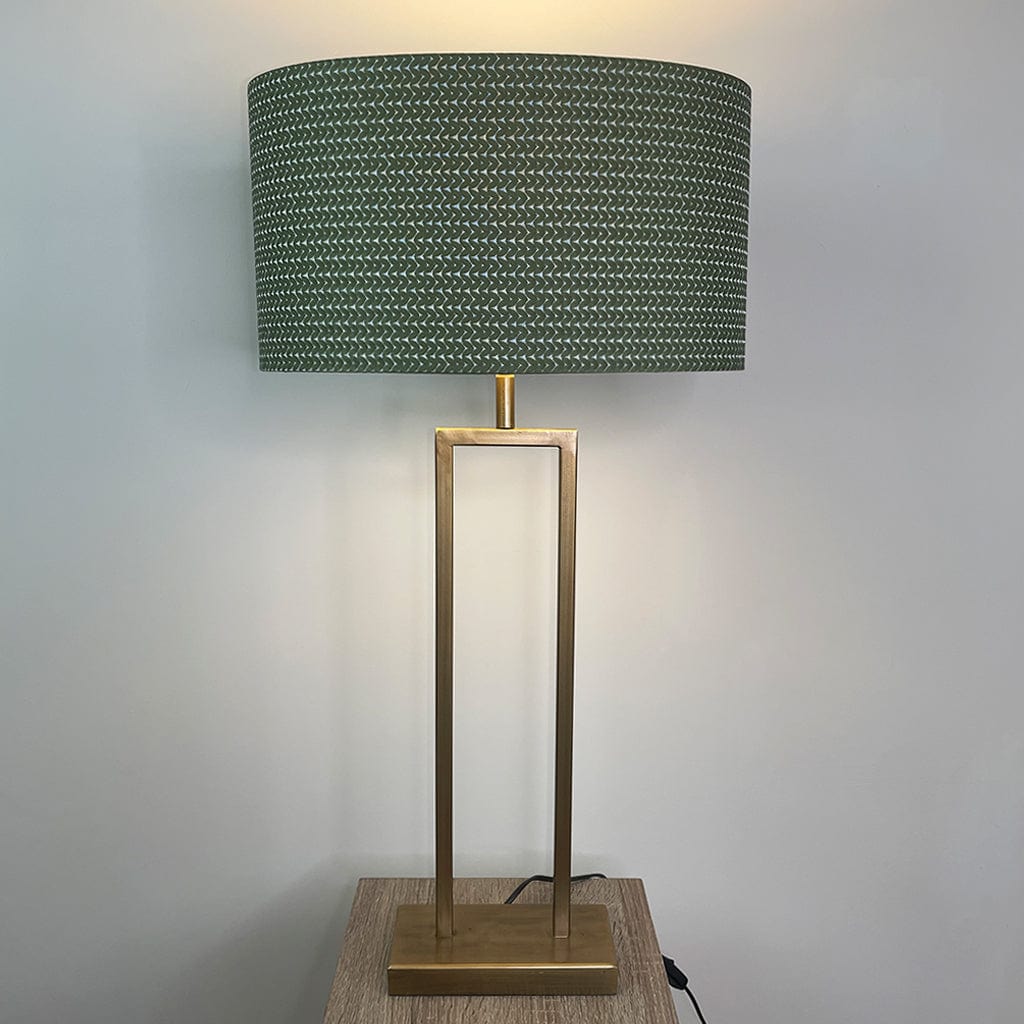 Table lamp with a green textured shade and gold base on a wooden stand against a plain background