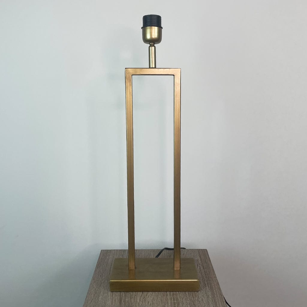 Gold table lamp with a black base on a wooden surface against a light gray background