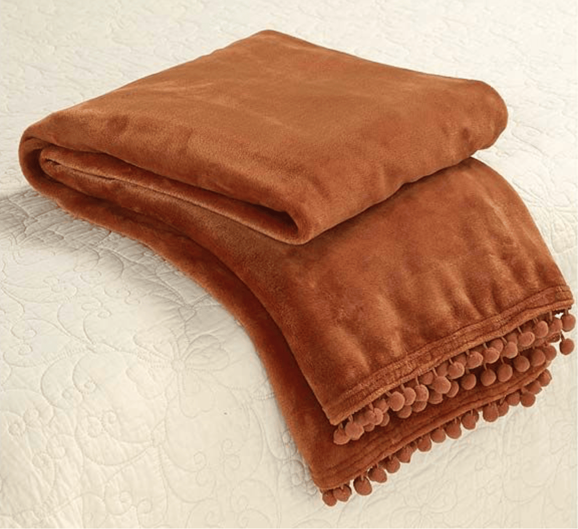 Spice Orange blanket with pom-pom trim on a textured surface