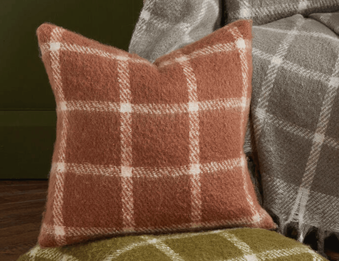 Plaid pillow and blanket on a chair with a green background
