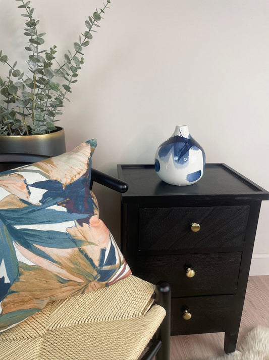 Black nightstand with a decorative vase next to a chair with a floral cushion