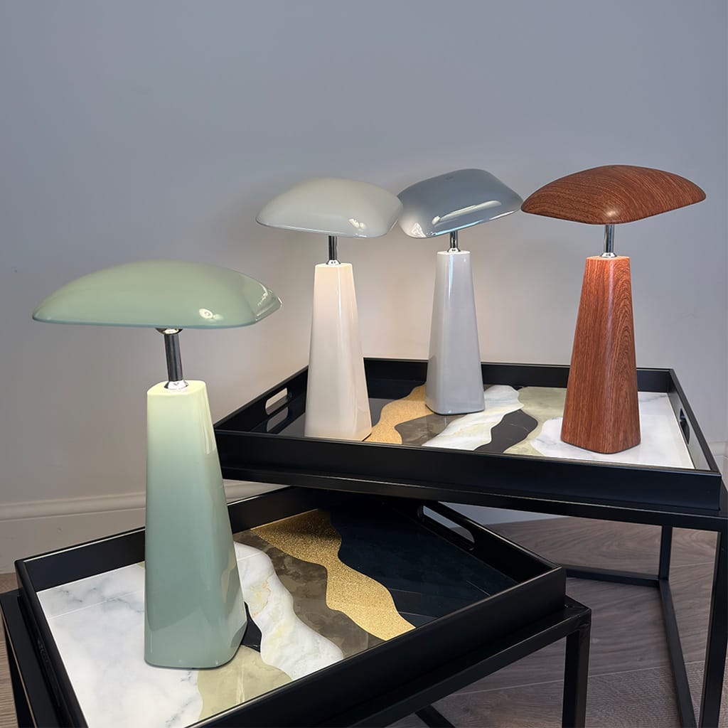 Four table lamps with different designs on a black tray against a gray wall.