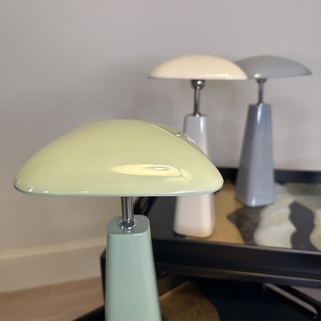 Light green table lamp on a reflective surface with two other lamps in the background.
