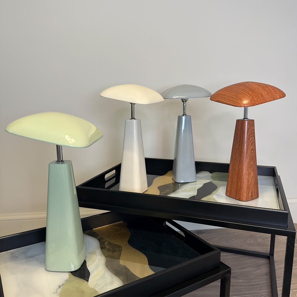 Four table lamps with different colored bases on a reflective surface.