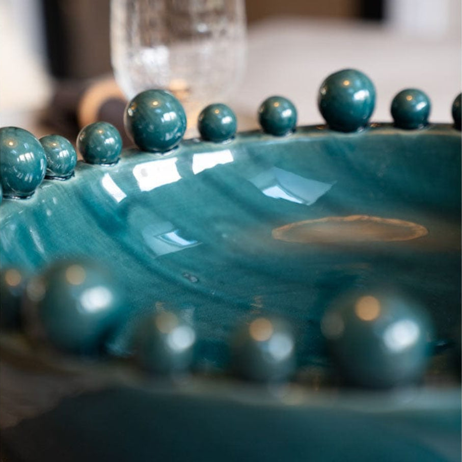 Teal ceramic dish with spherical embellishments on a blurred background