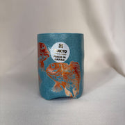 Blue cylindrical container with orange fish design and 'Made in Japan' label on a light gray background