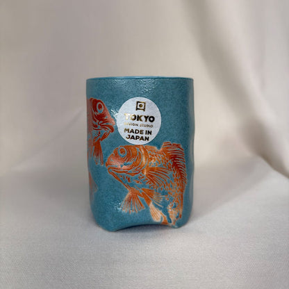 Blue cylindrical container with orange fish design and 'Made in Japan' label on a light gray background