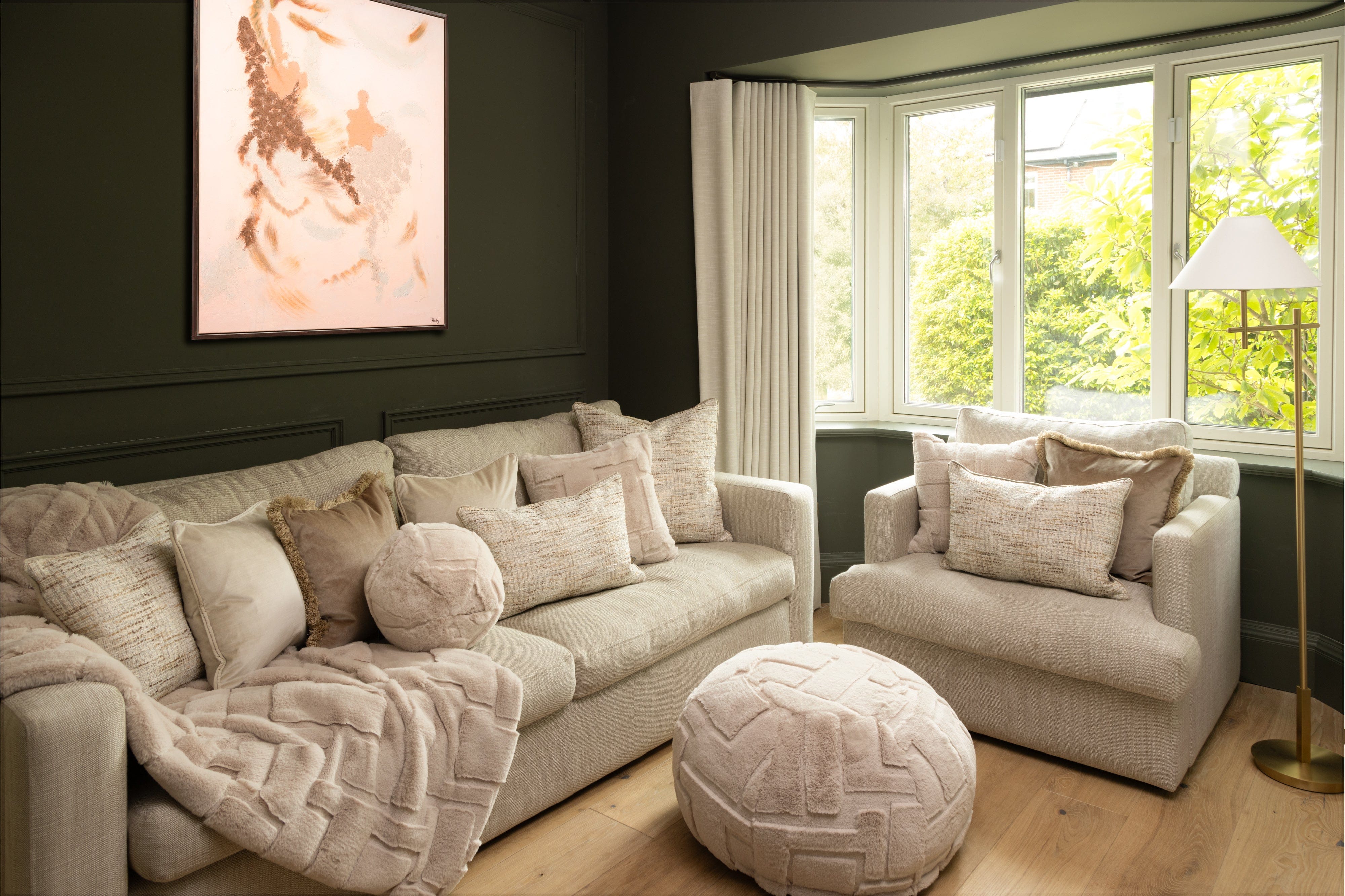 Living room with beige sofa, armchair, and ottoman with decorative pillows.