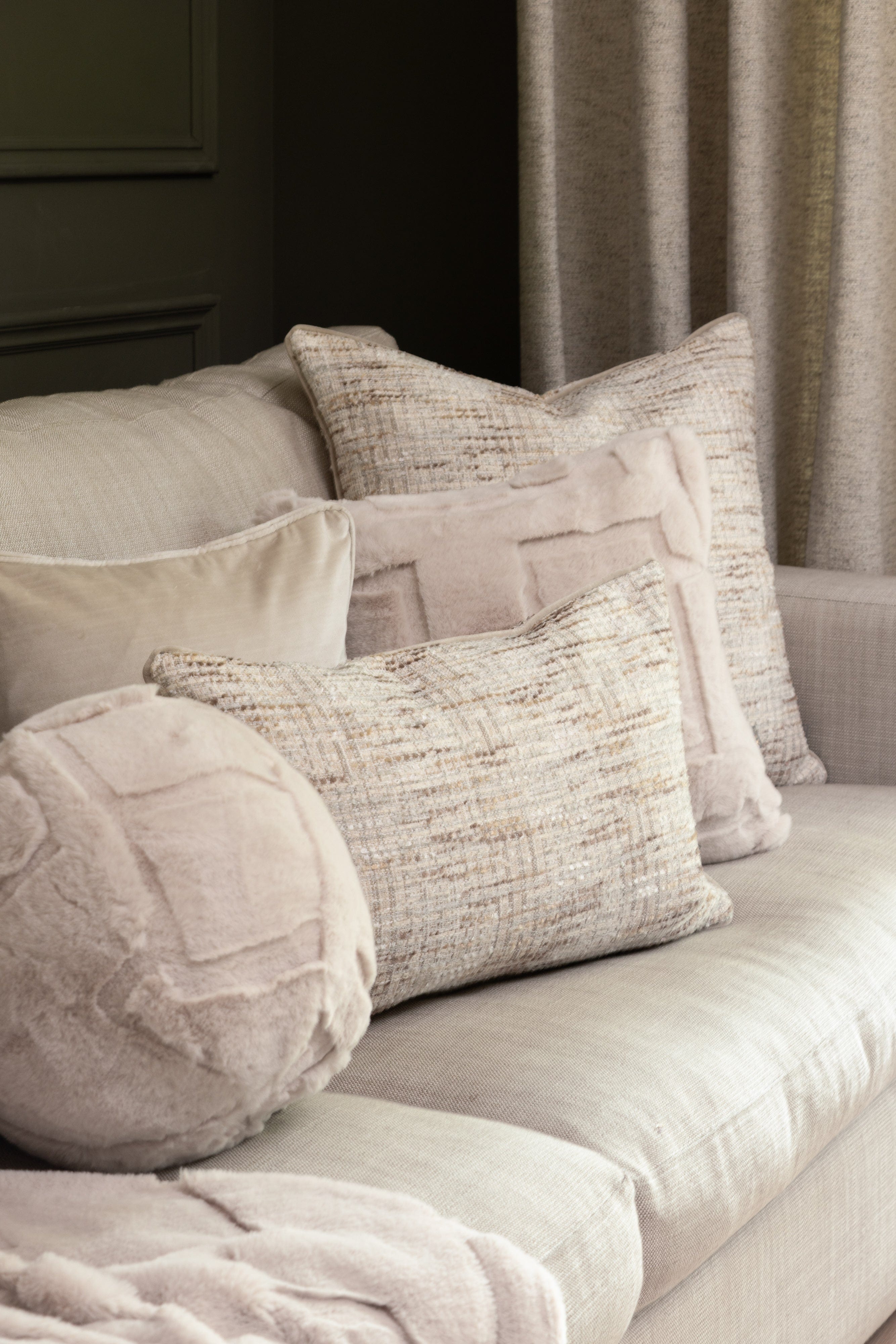 A lifestyle image showing a series of natural coloured, soft fluffy cushions on a beige sofa