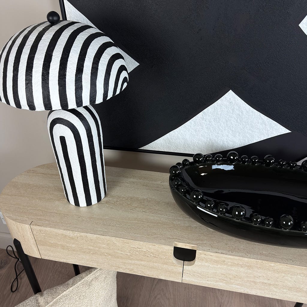 Black and white striped lamp on a wooden surface with a black decorative plate.