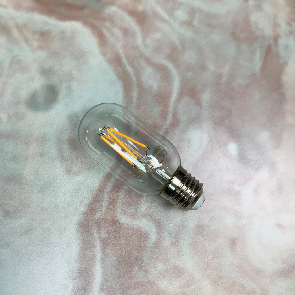A clear tubular LED light bulb with visible filament, placed on a marble-like surface.