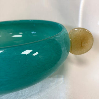 Teal ceramic bowl with a gold decorative element on a white background