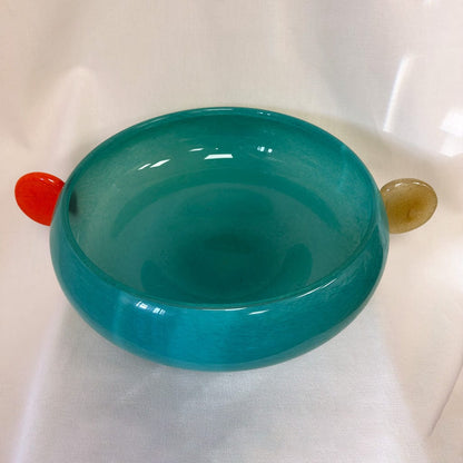 Teal bowl with a red and gold object on a white background