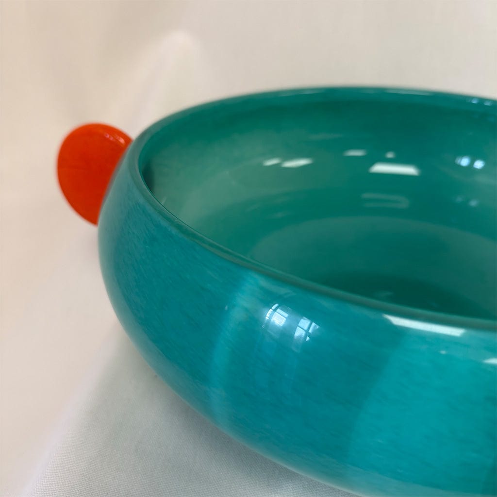 Teal bowl on a beige surface with an orange object partially visible