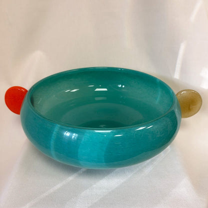 Teal glass bowl with red and gold accents on a white background