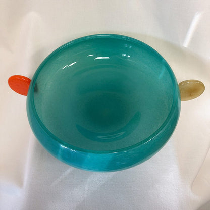 Teal bowl with a red handle on a white surface