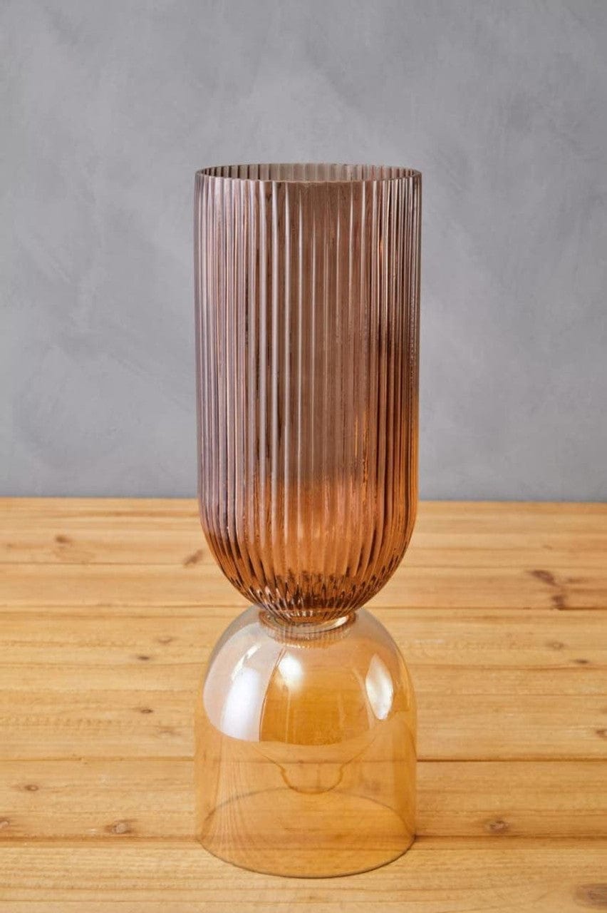 Tall ribbed glass vase on a wooden surface with a gray background