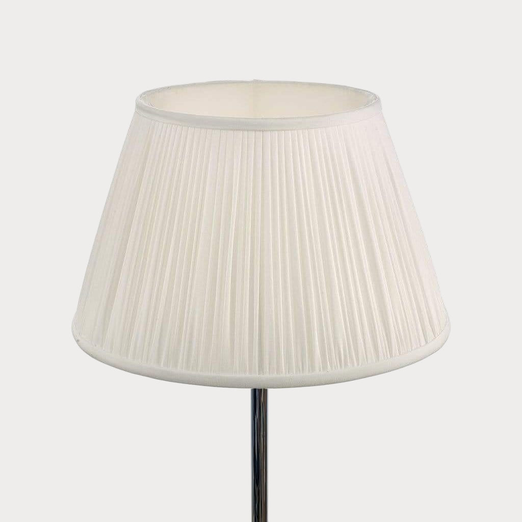 A white pleated shade on a lamp post, designed with a matching ivory lining.