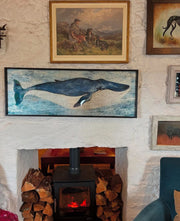 Framed artwork of a whale above a fireplace with wooden logs.