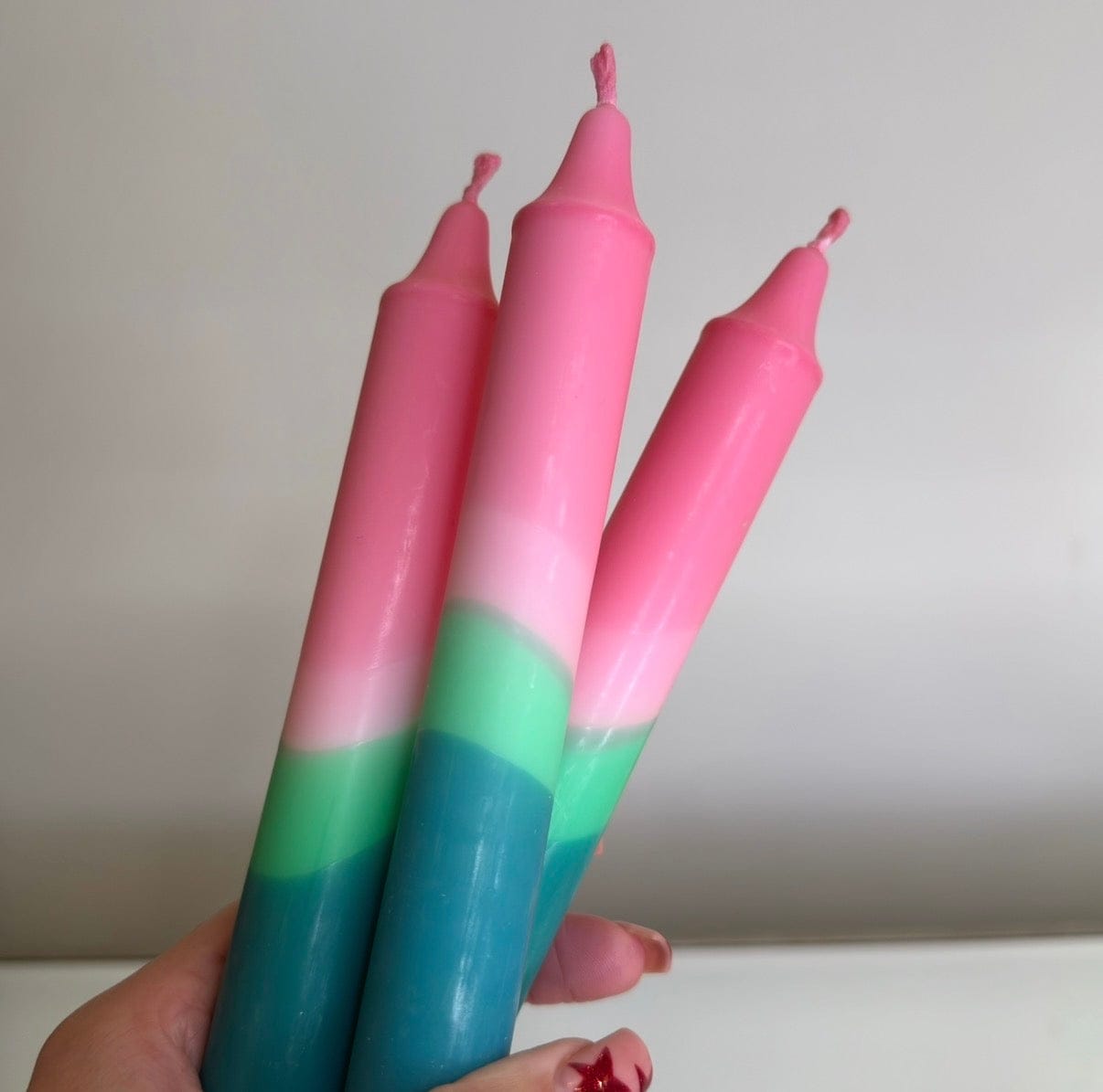 Three colorful candles with pink and green gradient held by a hand against a plain background