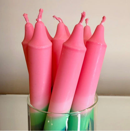 Pink candles with green bases in a glass holder against a beige background