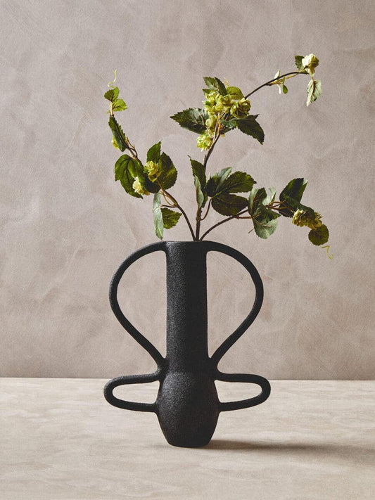 Black vase with green leaves on a beige background
