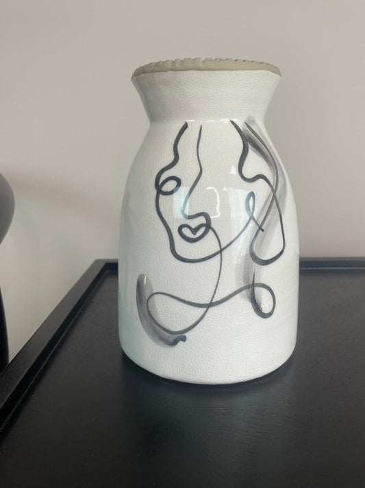 White ceramic vase with black line art design on a dark surface