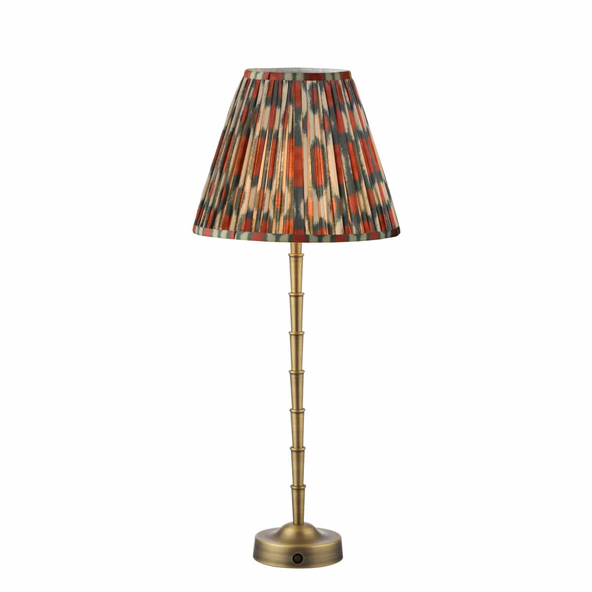 A Wyman rechargeable table lamp with a matt antique brass base and bamboo-style stem. It has a red and green ikat patterned shade with pleats and a hand-pleated design.