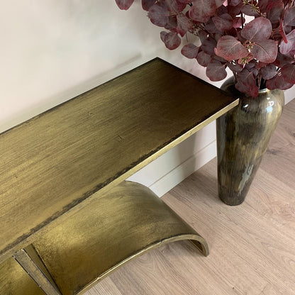 Gold textured console table next to a vase with red flowers on a wooden floor.