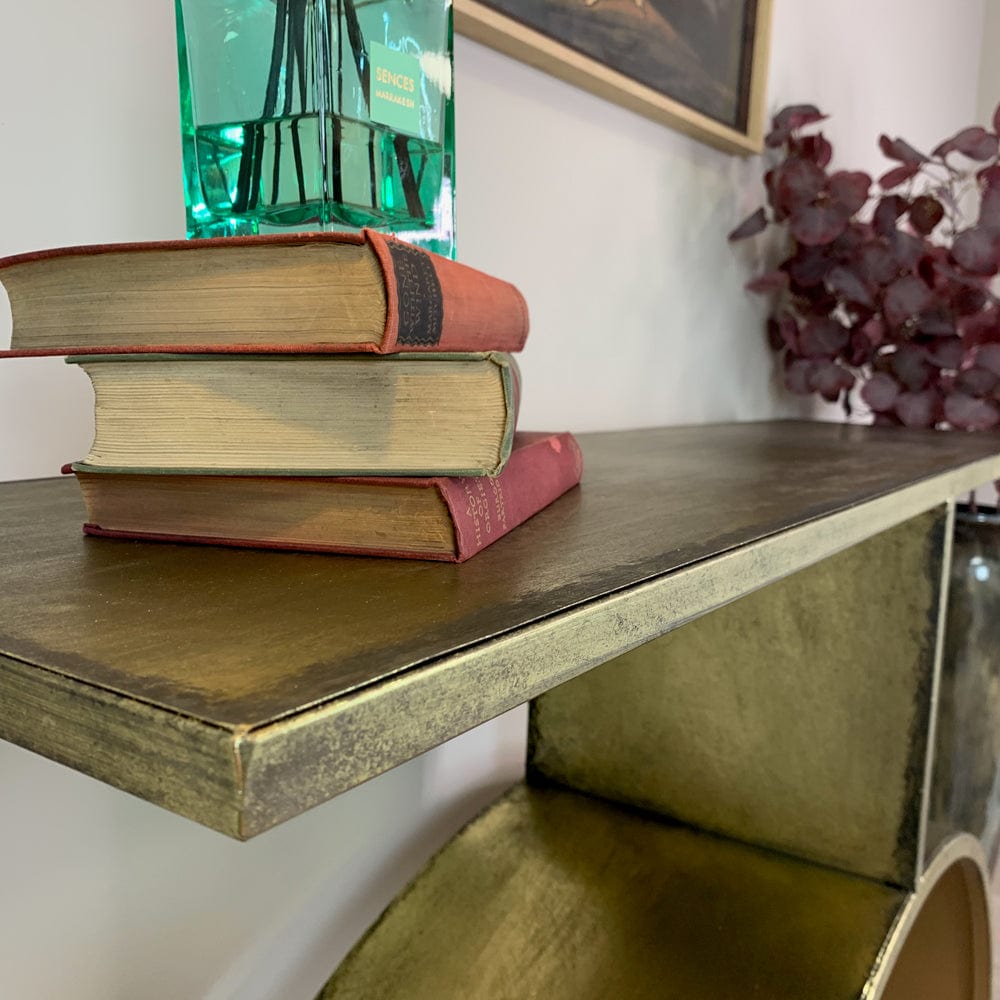 Stack of books on a metal gold console shelf with a plant in the background