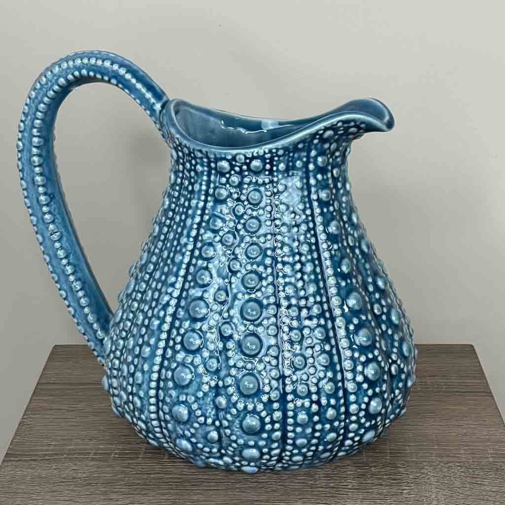 A large blue ceramic jug with a textured surface, resembling the form of a sea urchin, displayed on a wooden surface.