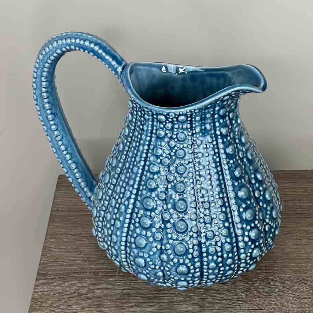 A large blue ceramic jug with a textured surface, resembling the form of a sea urchin, displayed on a wooden surface.