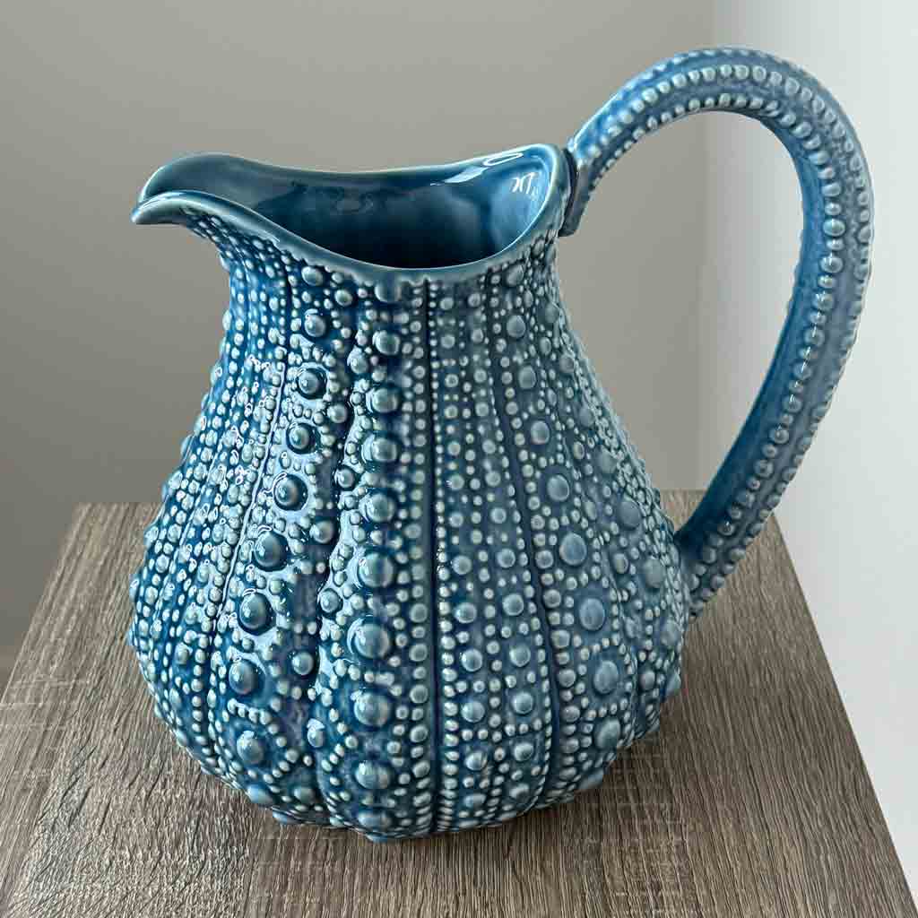 A large blue ceramic jug with a textured surface, resembling the form of a sea urchin, displayed on a wooden surface.