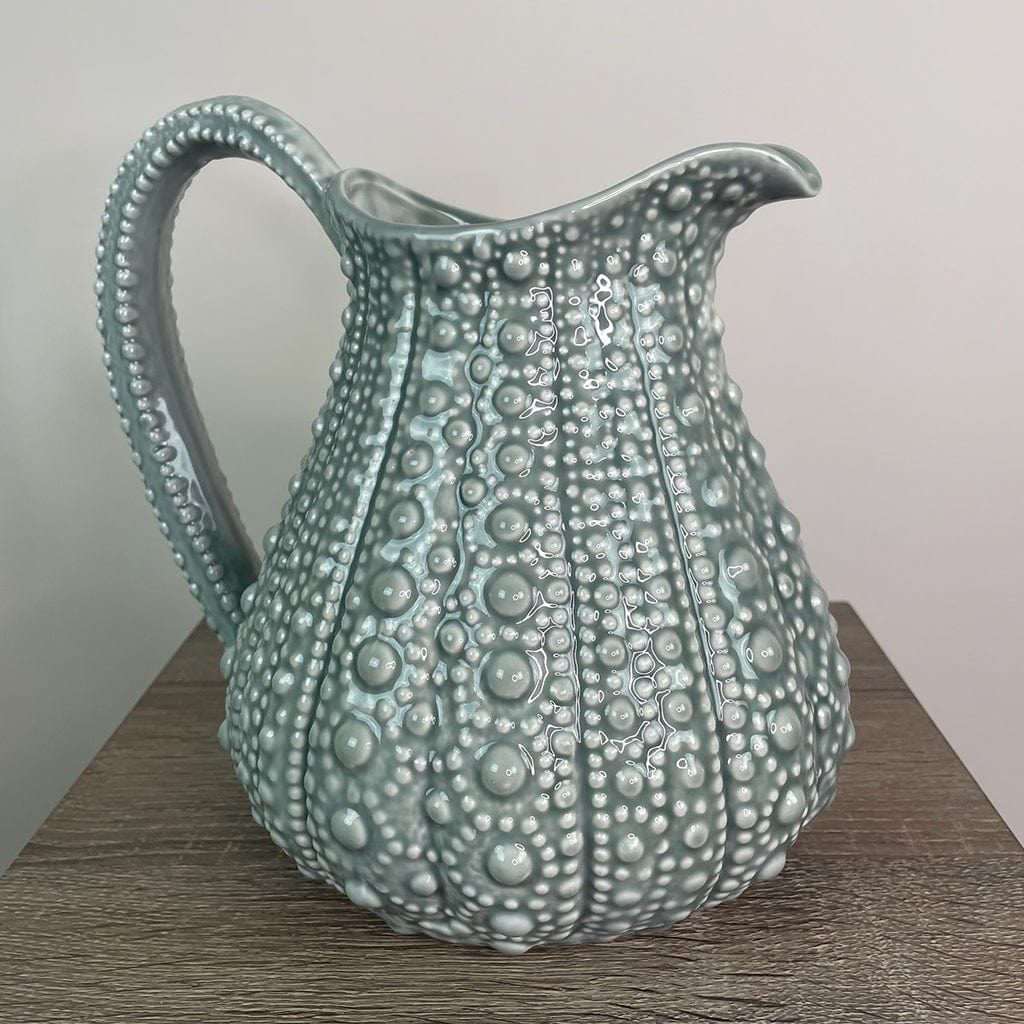 A large grey ceramic jug with a textured surface, resembling the shell of a sea urchin, displayed on a wooden surface.