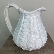 A large white ceramic jug with a textured surface, resembling the shell of a sea urchin, displayed against a neutral background.