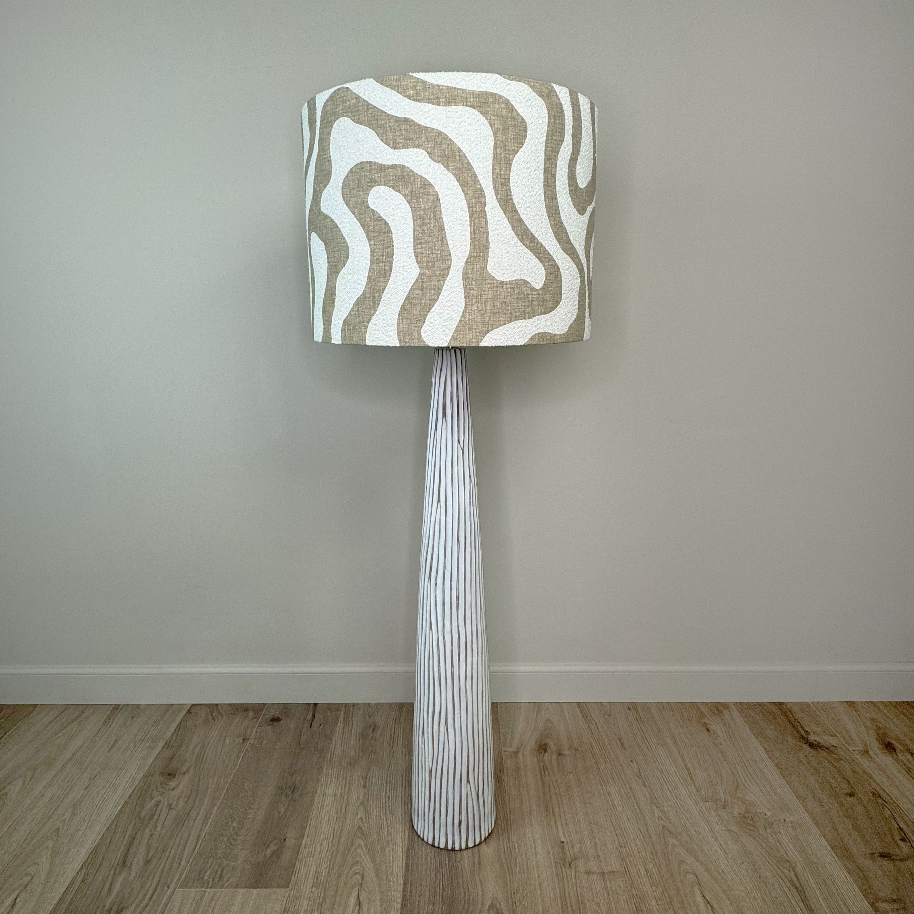 A white wood effect floor lamp with a beige and white striped boucle shade.