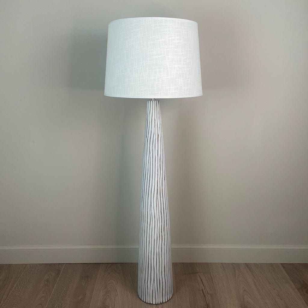 A white wood effect tall and slim floor lamp with a large white linen shade and the light is off